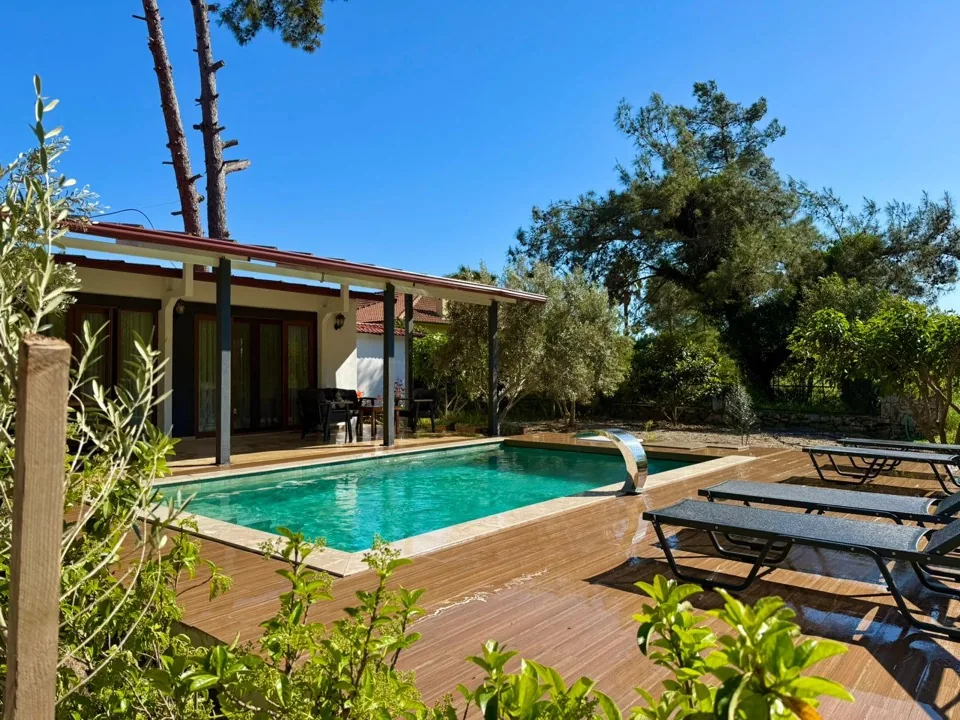 Villa Zeytin'in uzun havuzu, ahşap güneşlenme terası ve arkada kırmızı çatılı tek katlı villa